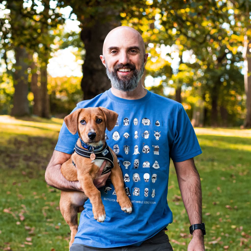 Steve wearing the Reality is ... sci-fi t-shirt in bright blue, holding his dog Bear