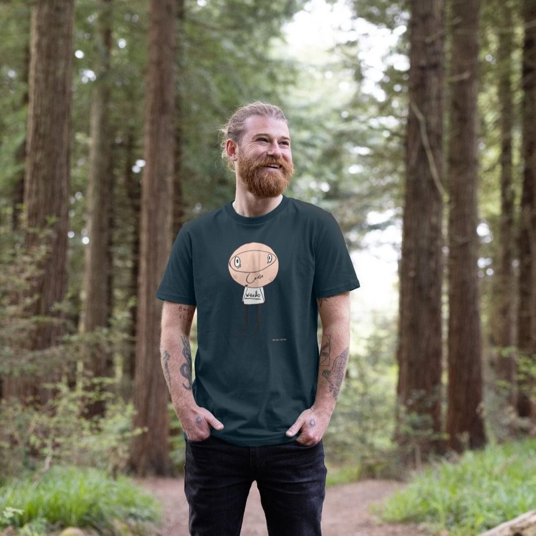 Man wearing a Denim Blue Weirdo organic cotton t-shirt, standing in a forest clearing.