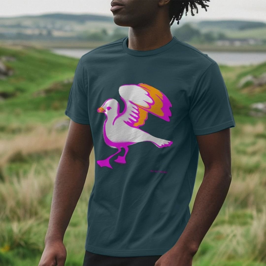 Man wearing a denim blue Hotwells Flapper organic cotton t-shirt, standing in the countryside near the sea.