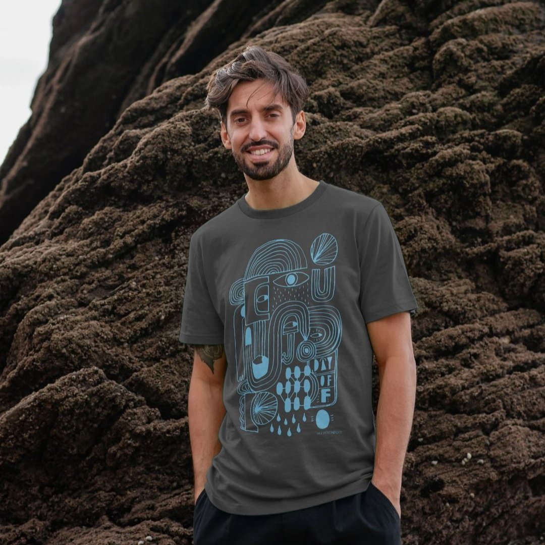 man stood on a beach  in front of rocks wearing a Slate Grey Day Off organic cotton t-shirt